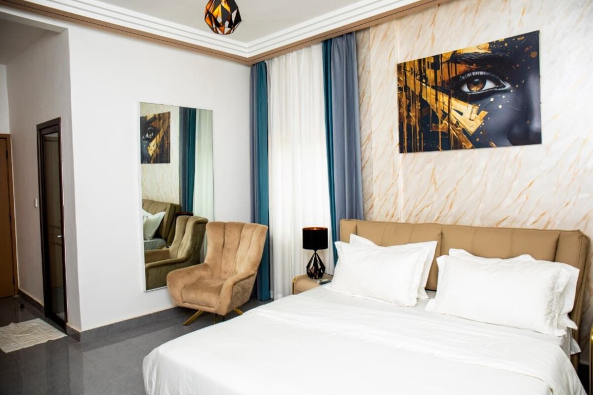Et hotelværelse med en stor seng, en stol, et spejl og et billede på væggen.