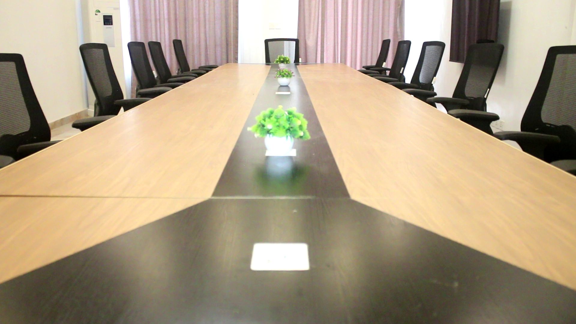 Un salón de conferencias con una mesa larga, sillas negras y una planta en maceta.