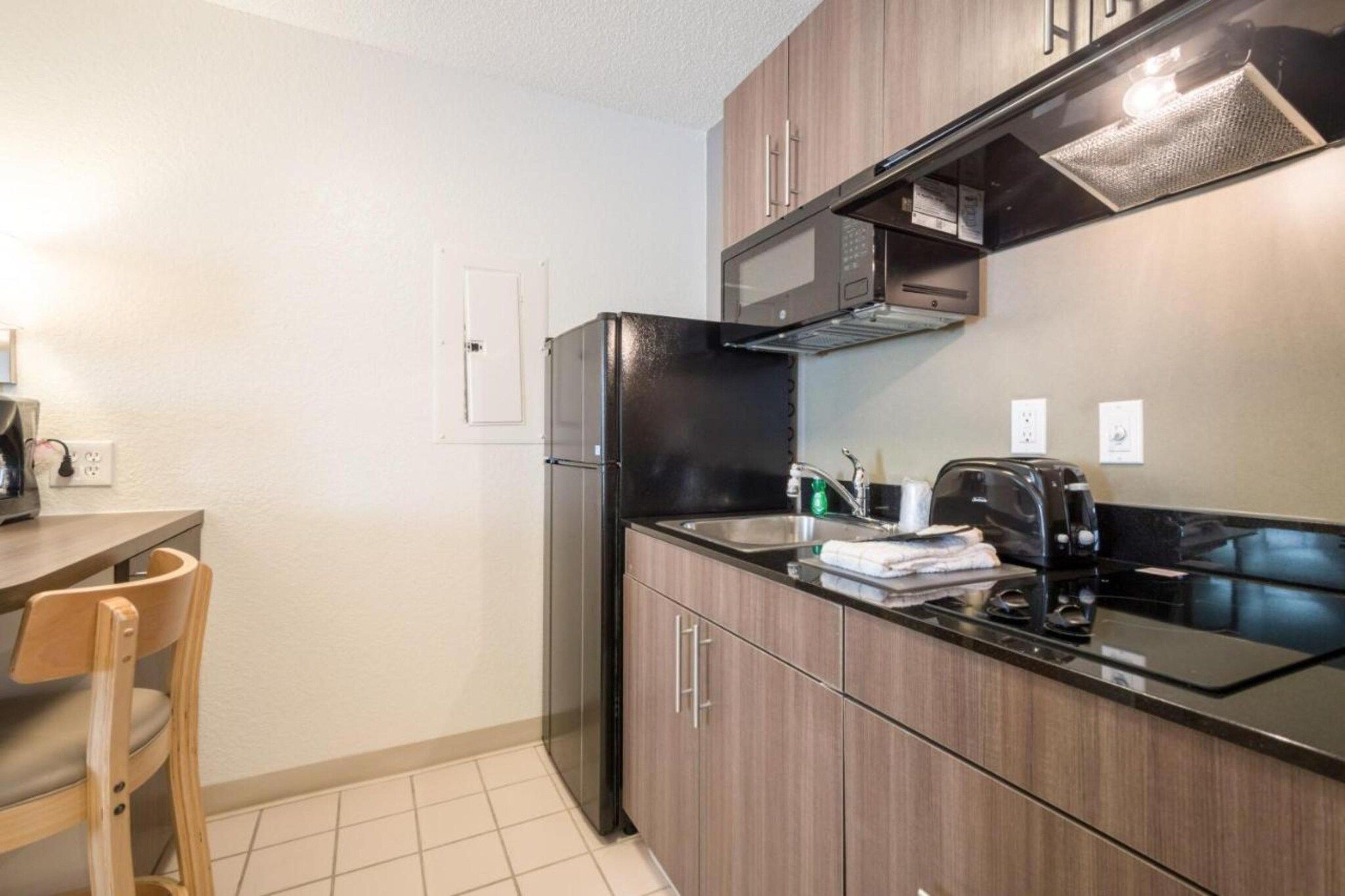 Una cocina compacta con un refrigerador negro, muebles de madera, un lavamanos de acero inoxidable y una cafetera.