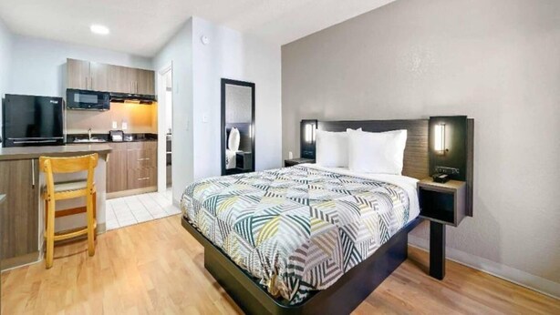 A hotel room with a bed, bedside tables, a desk with a chair, a kitchenette, and a bathroom.