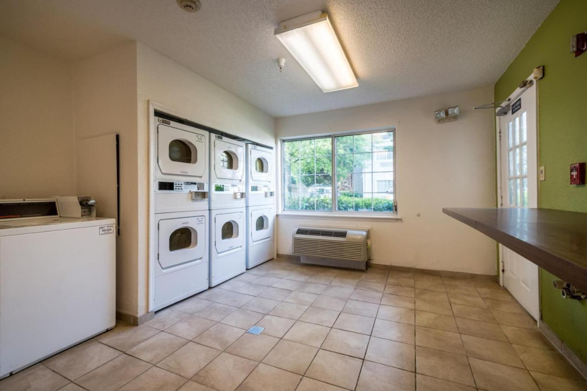 A laundry room with stacked washers and dryers, a window, and a vent.