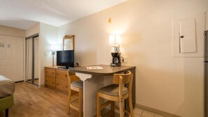 A compact kitchenette with a sink, a coffee maker, a television, and two chairs.