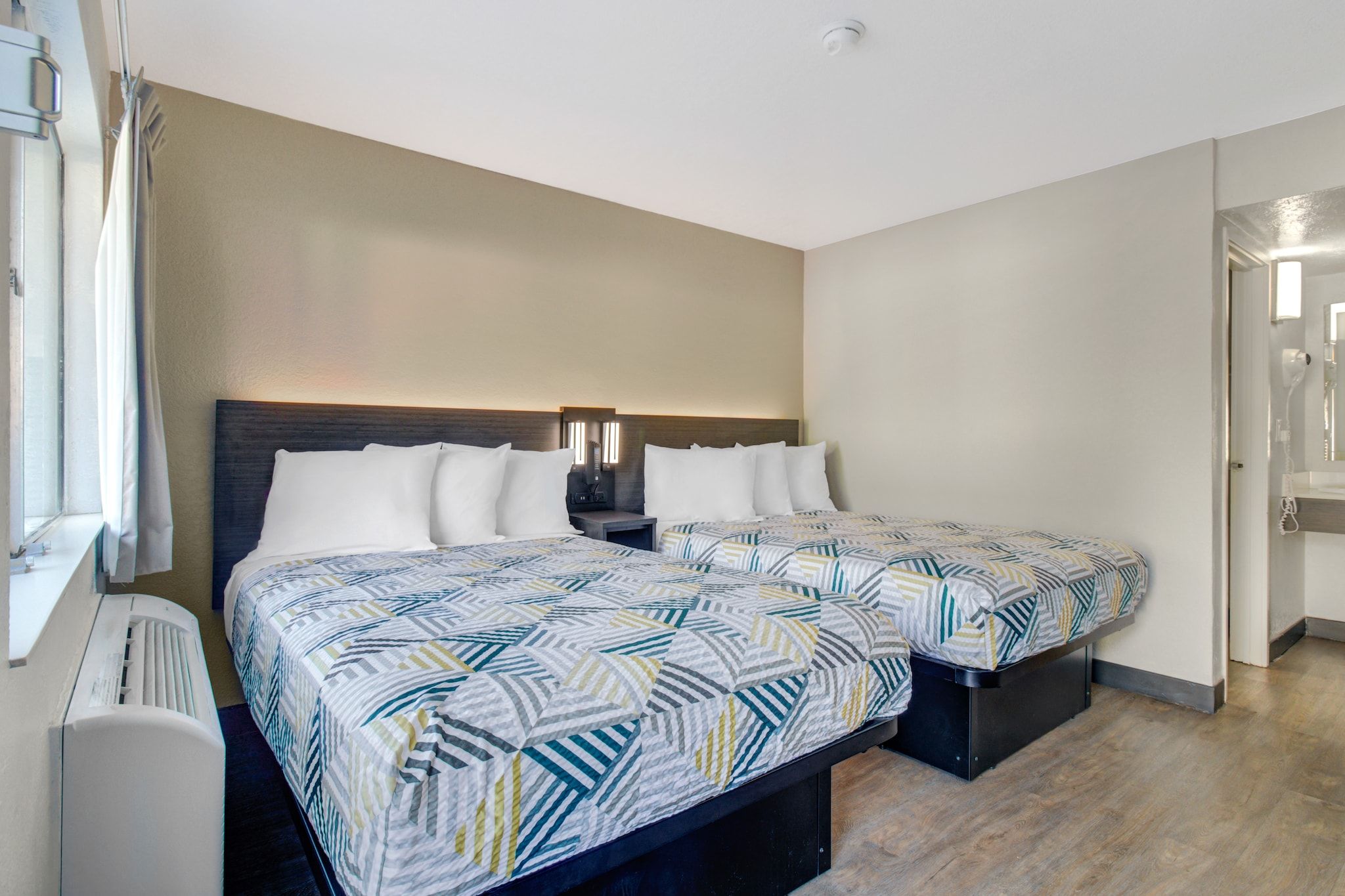 Een hotelkamer met twee bedden, een nachtkastje, een verwarming en een raam met gordijnen.