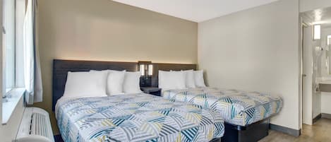 Quarto de hotel com duas camas, uma mesinha de cabeceira, aquecedor e uma janela com cortinas.