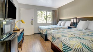 A hotel room with a bed, a desk with a television, a lamp, and a window with curtains. - 1 Full Bed | Premium, Mini Fridge (Venice)