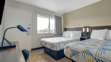 Een hotelkamer met twee bedden, een bureau, een stoel, een raam met gordijnen en een lamp.