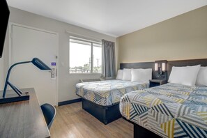 Ein Hotelzimmer mit zwei Betten, einem Schreibtisch, einem Stuhl, einem Fenster mit Vorhängen und einer Lampe.