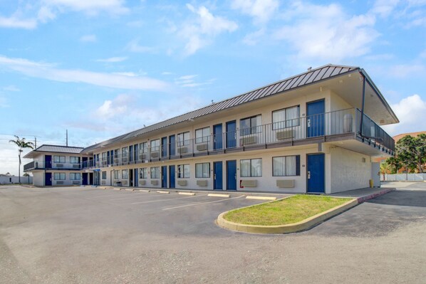 Ein Motel mit einer zweistöckigen Struktur, mehreren Zimmern und einem Parkplatz.