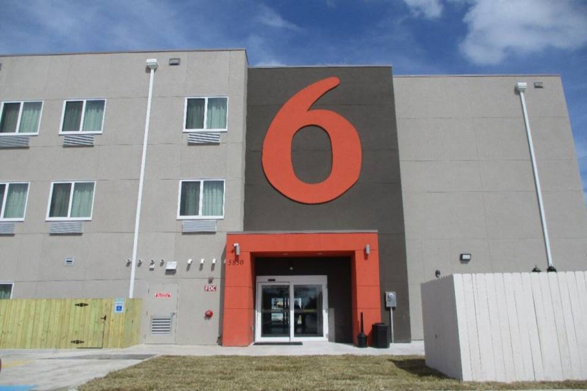 Un edificio moderno con un grande cartello con il numero 6, un ingresso con cancello e numerose finestre.