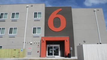 Un edificio moderno con un grande cartello con il numero 6, un ingresso con cancello e numerose finestre.