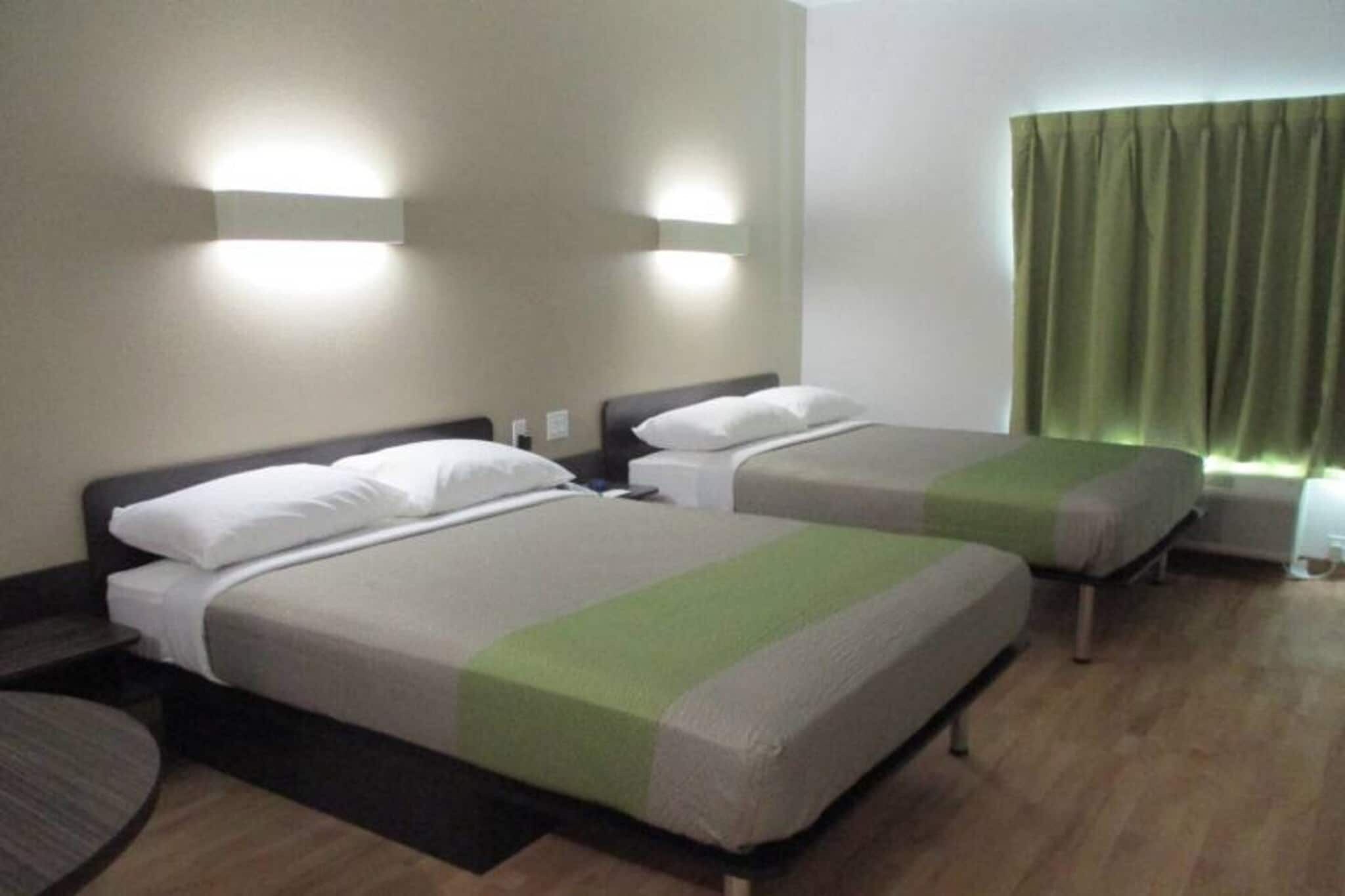Een hotelkamer met twee bedden, een tafeltje en een raam met gordijnen.