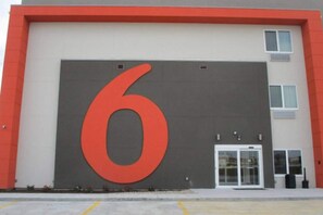 Een gebouw met een groot rood cijfer '6' op de gevel, een witte deur en een klein raam.