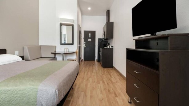 A hotel room with a bed, a television on a dresser, a small table with a chair, and a door leading to a bathroom. - 1 King Bed|Hearing Accessible,Kitchen (Corpus Christi TX)