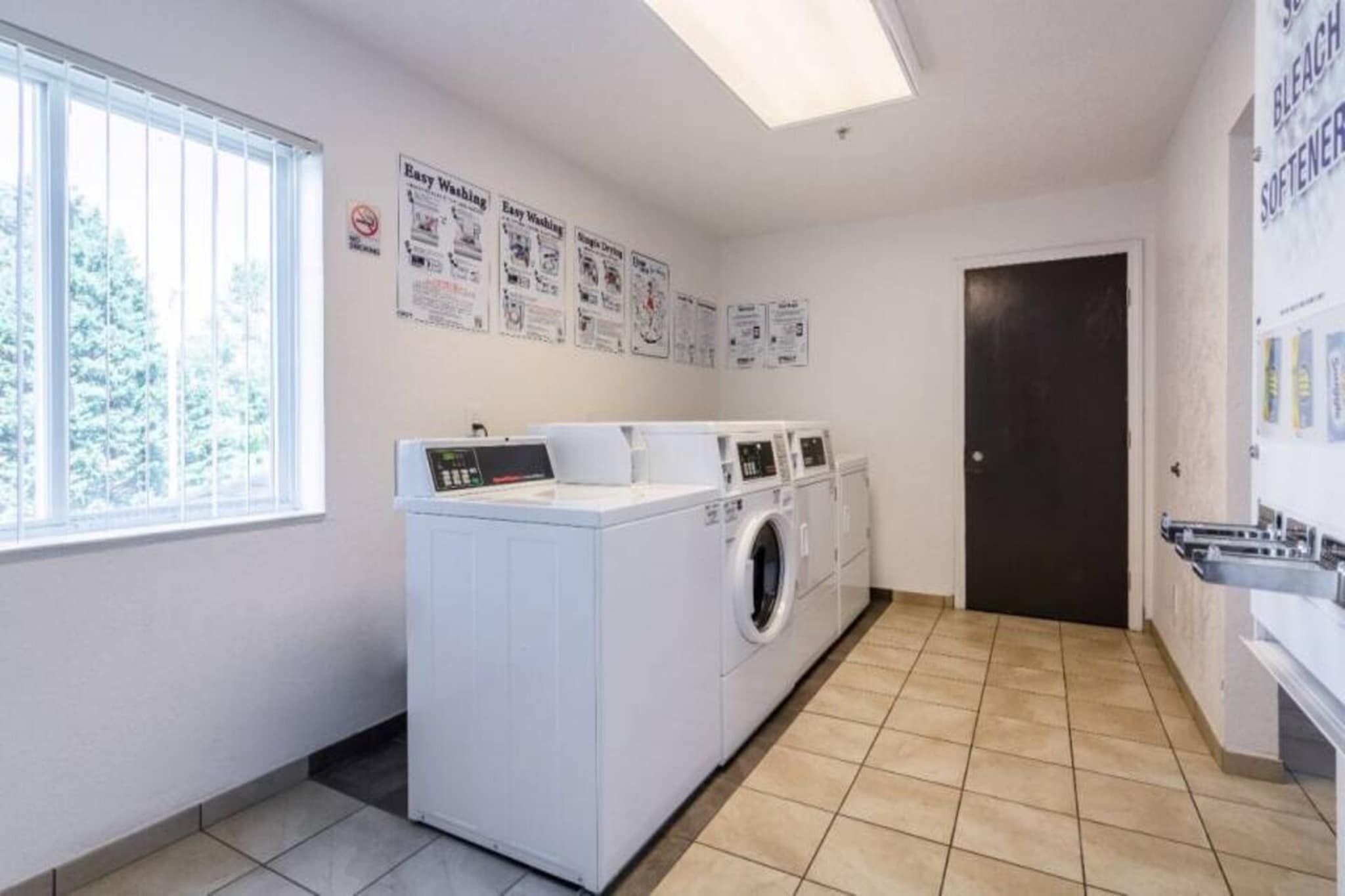 Een wasserette met een wasmachine, droger en een deur naar een andere ruimte.