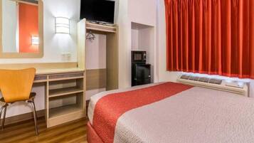 Una habitación de hotel con cama, escritorio, silla, televisor, cafetera y ventana con cortinas.