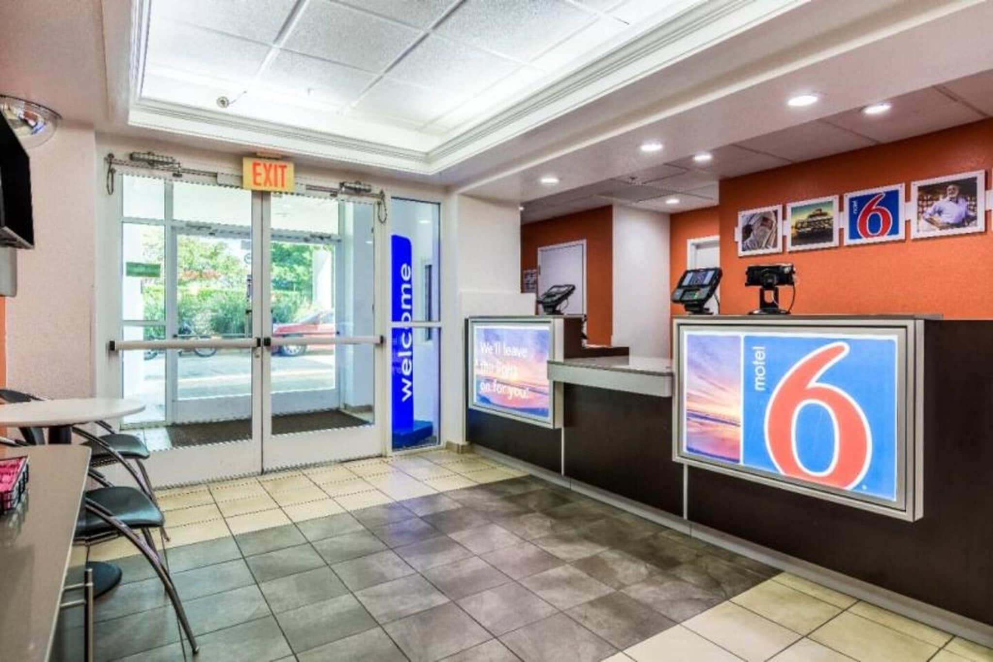 Een hotel receptie met een glazen deur, een digitaal scherm en een balie met een groot nummerbord.