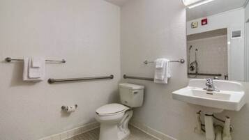 A standard hotel bathroom with a toilet, handrails, a sink, and a mirror.
