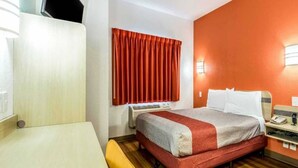 Una camera d'albergo con un letto, un comodino e una finestra con tende.