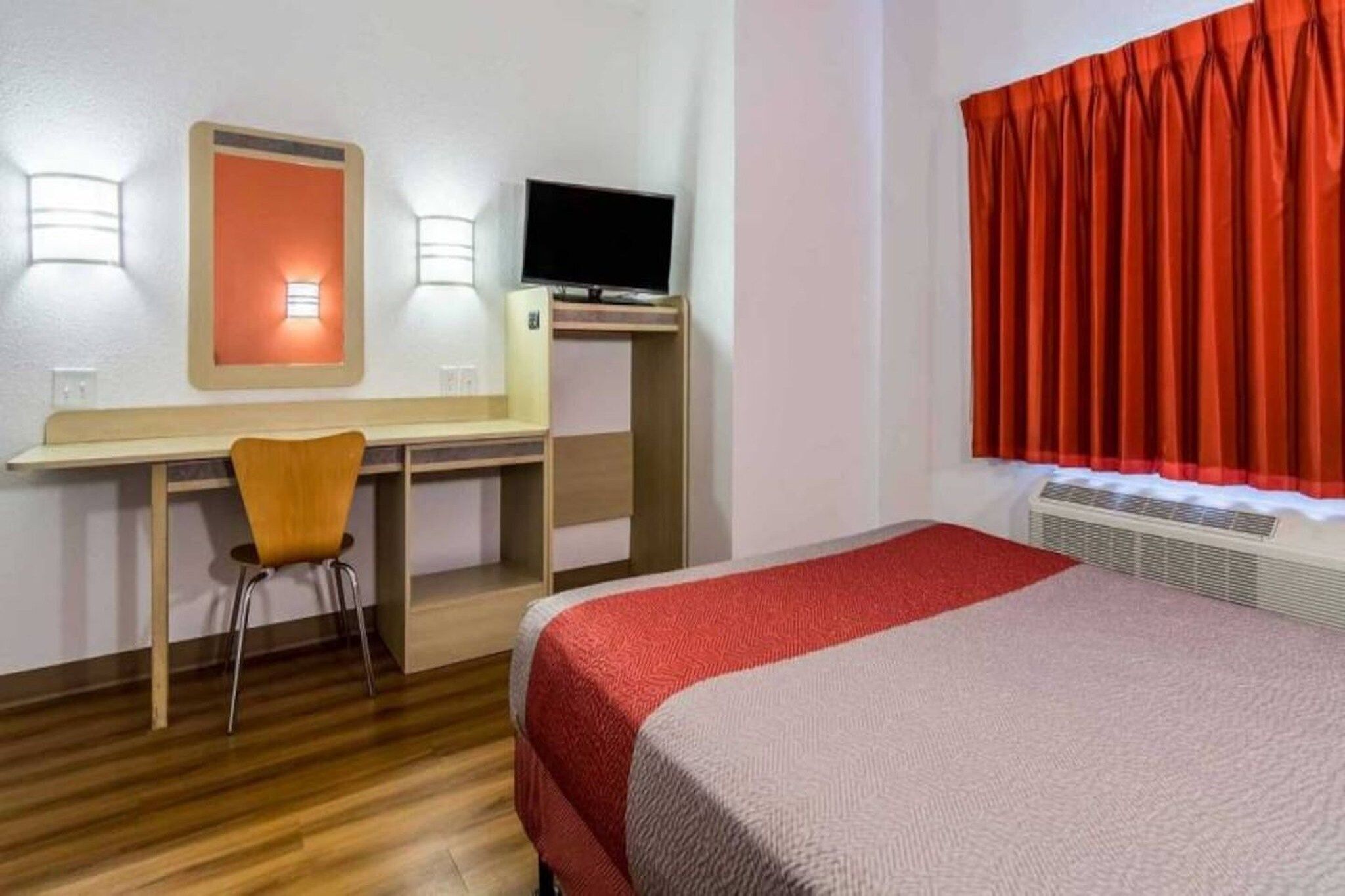 A hotel room with a bed, desk, chair, and a television.