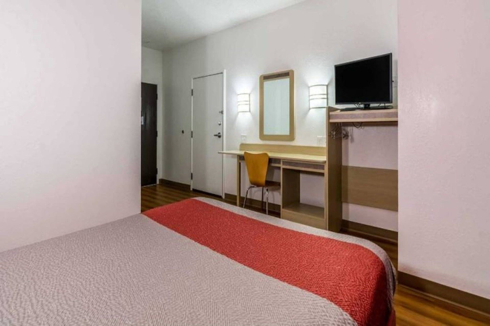 Een hotelkamer met een bed, bureau, stoel, televisie en een deur.
