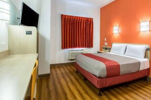 A hotel room with a bed, a desk, a television, a window with curtains, and an air conditioning unit. - 1 Full Bed | Mobility Acc Tub Smk Micfridg (Fort Mill)