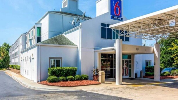Motel 6 con entrada techada, antena parabólica y estacionamiento.