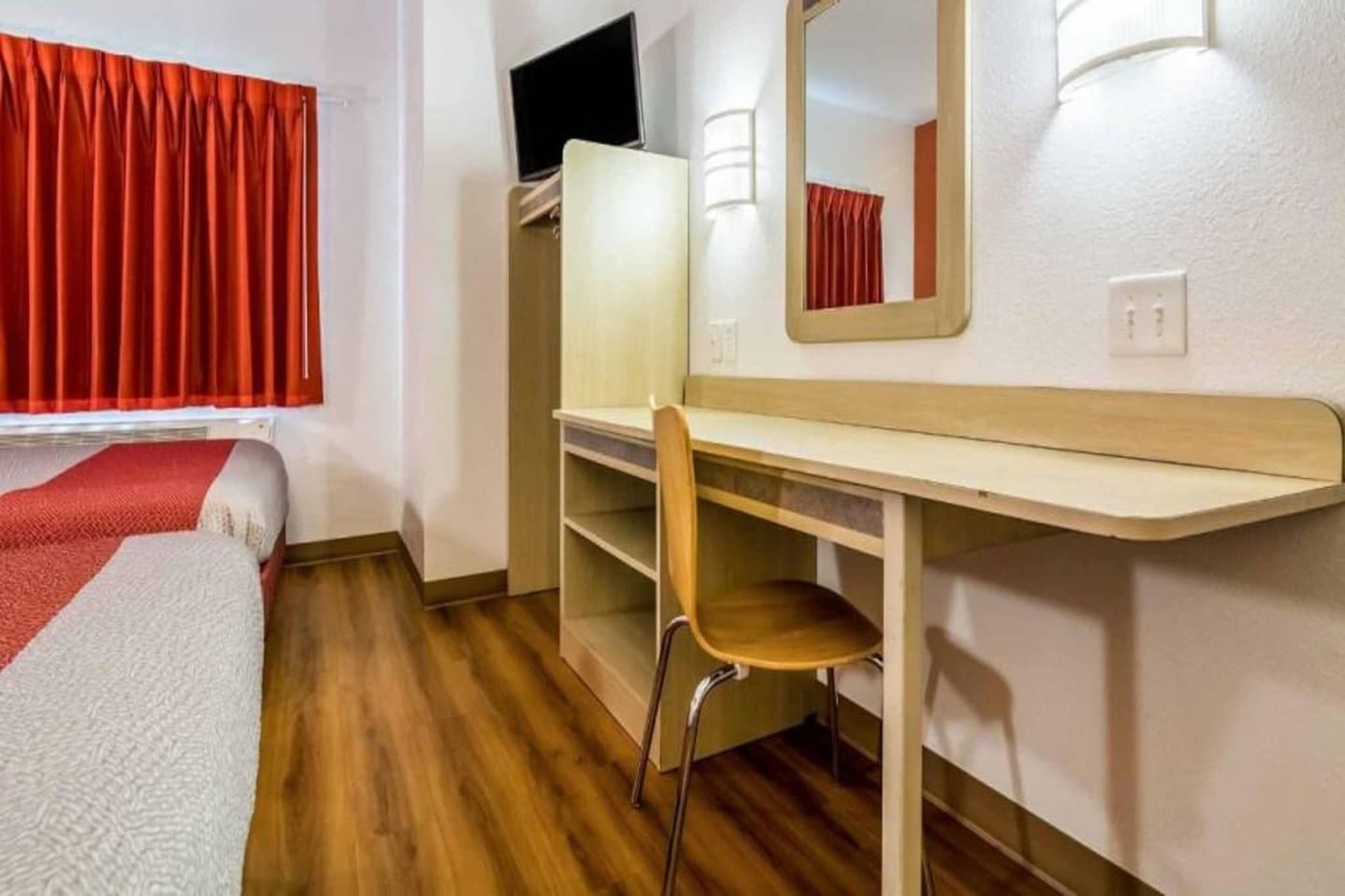 Een kamer met een bed, een bureau, een stoel, een spiegel en een raam met gordijnen.