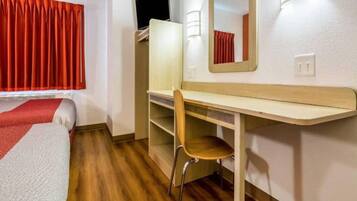 Een kamer met een bed, een bureau, een stoel, een spiegel en een raam met gordijnen.