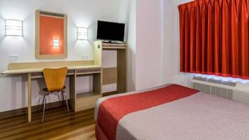 A hotel room with a bed, a desk, a chair, a television, and a window with curtains.