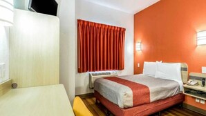 Una habitación de hotel con cama, mesita de noche y ventana con cortinas.