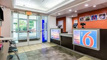 A hotel reception area with a glass door entrance, a digital display, and a counter with a sign indicating room number 6.