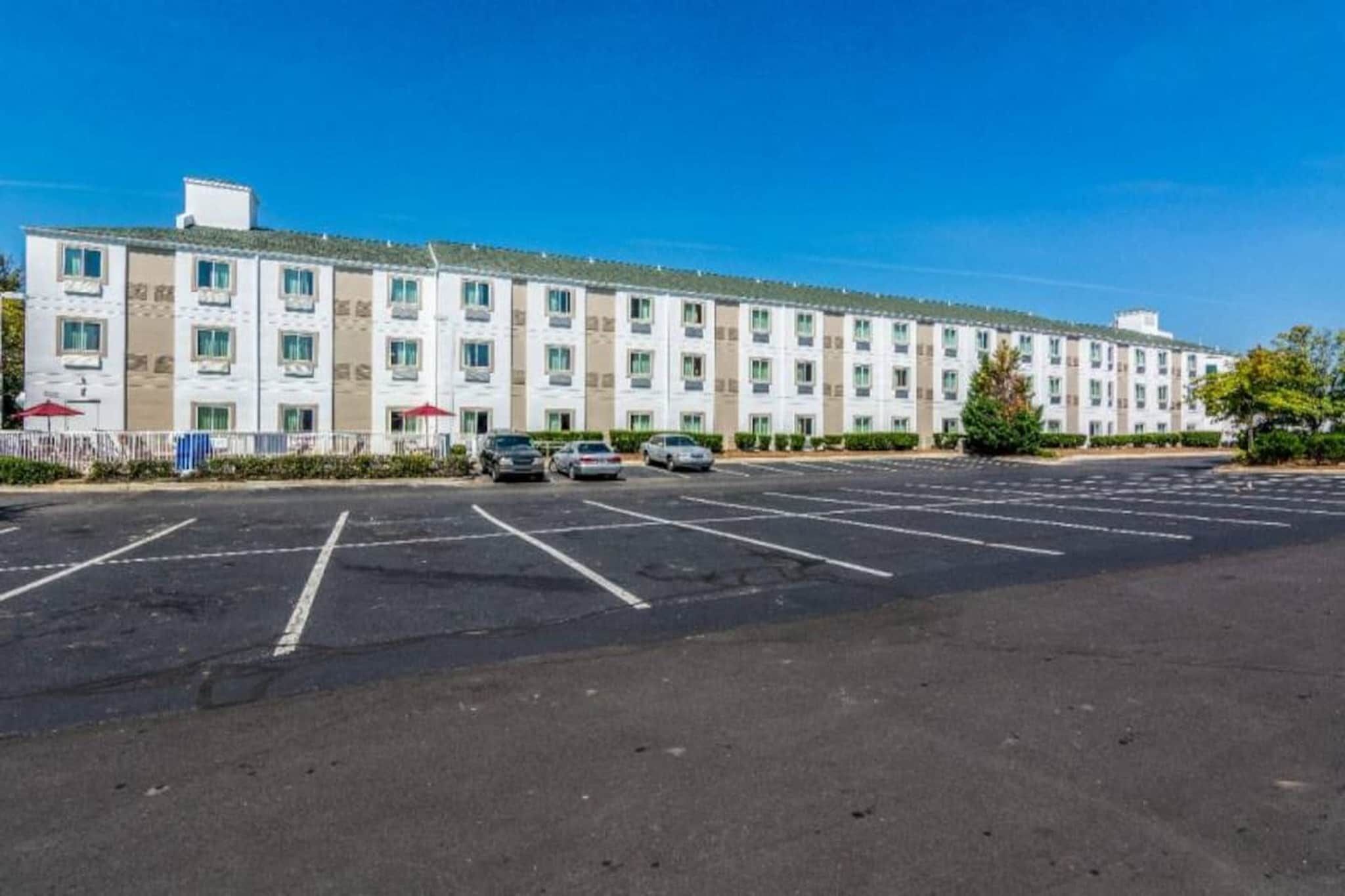 Een hotel met meerdere verdiepingen en een parkeerplaats ervoor.