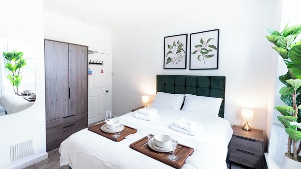 Quarto de hotel com cama, mesas de cabeceira, guarda-roupa e porta com cabideiro.