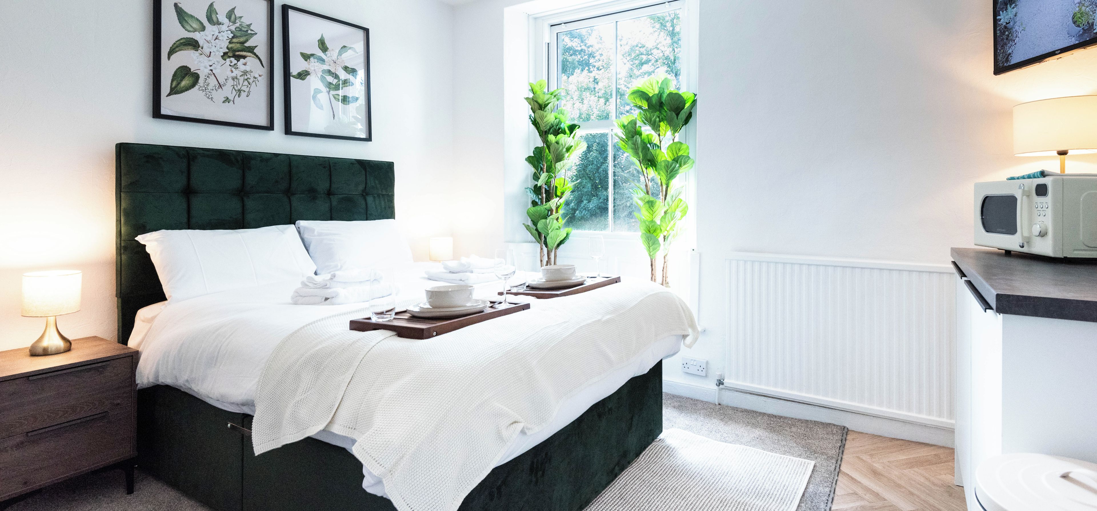 A neatly made bed with a white blanket, a bedside table with a lamp, and a tray with a glass of water and a bowl.