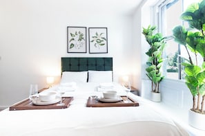 A hotel room with a neatly made bed, two framed botanical prints on the wall, a large potted plant by the window, and a tray with glasses and bowls. - The Stanley Arms Hotel by Guestz (Seascale)