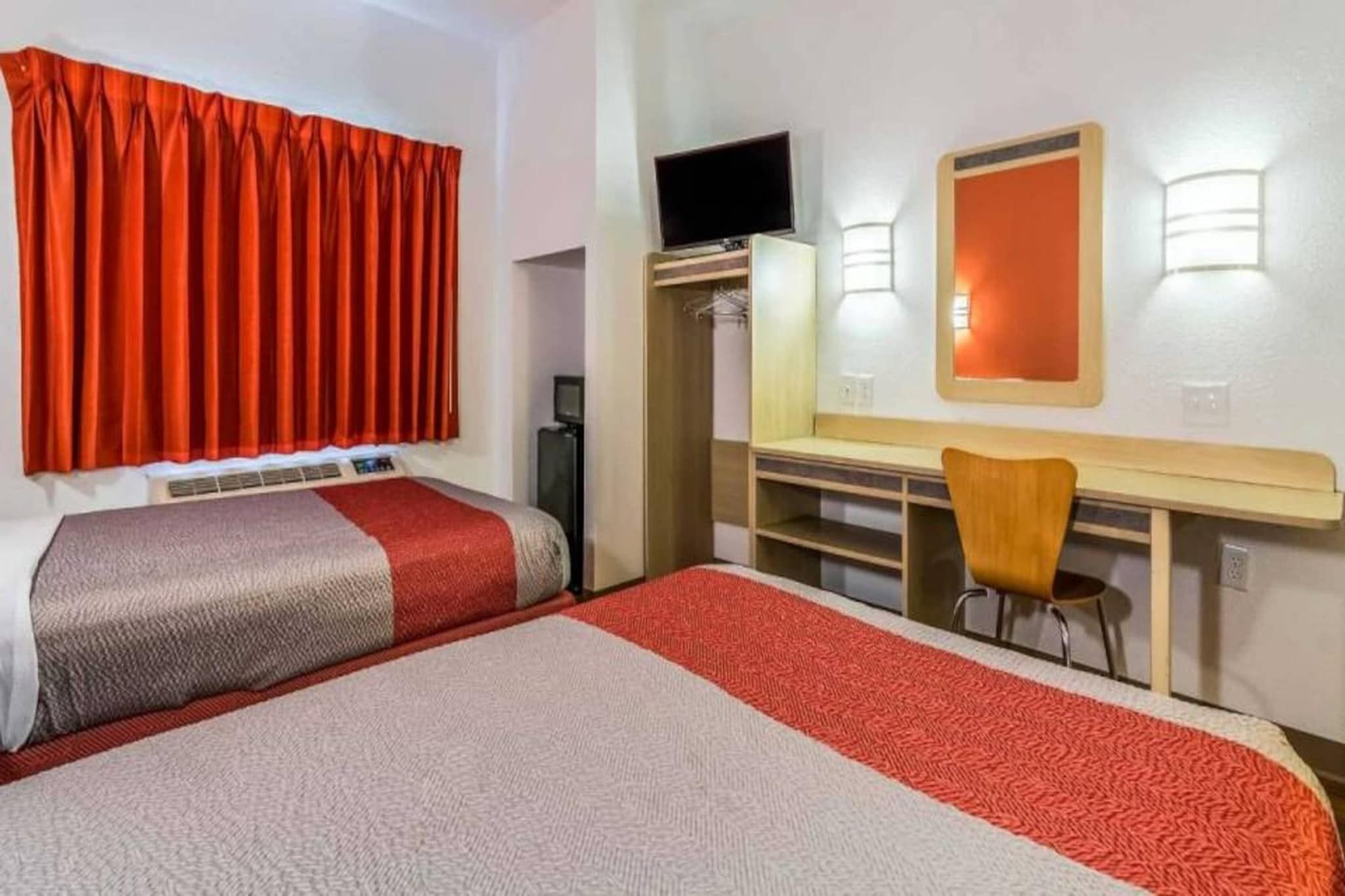 Een hotelkamer met een bed, een bureau met een stoel, een televisie en een kledingkast.
