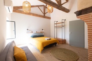 A bedroom with a bed, a bench, a hanging light, a wall with a geometric pattern, and a door.