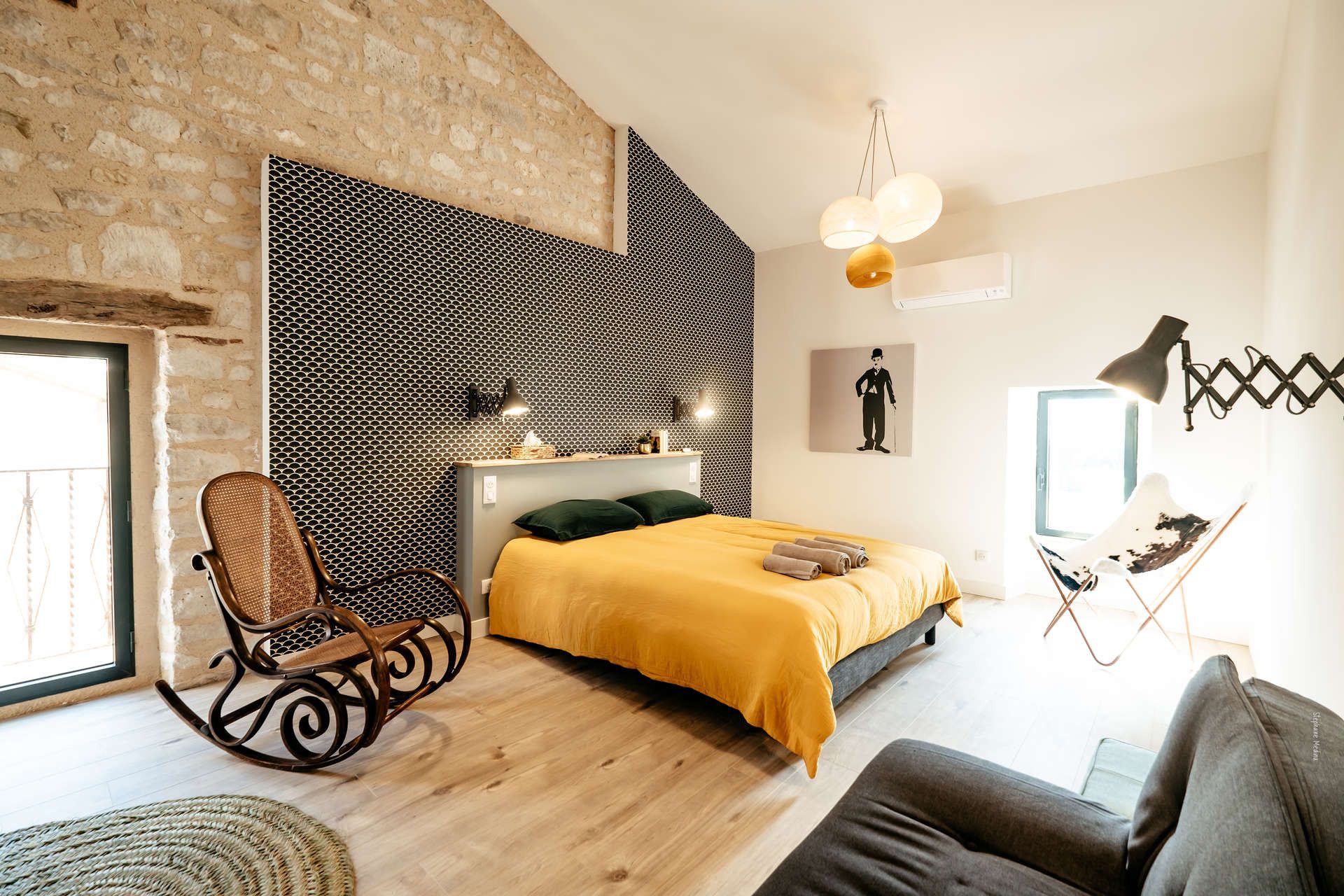 Una camera da letto moderna con un letto, una poltrona a dondolo, un divano e una parete con motivo geometrico.