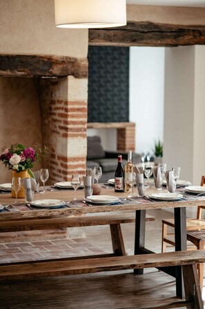 A dining table set with plates, glasses, and cutlery, with a bottle of wine and a vase of flowers on the table.
