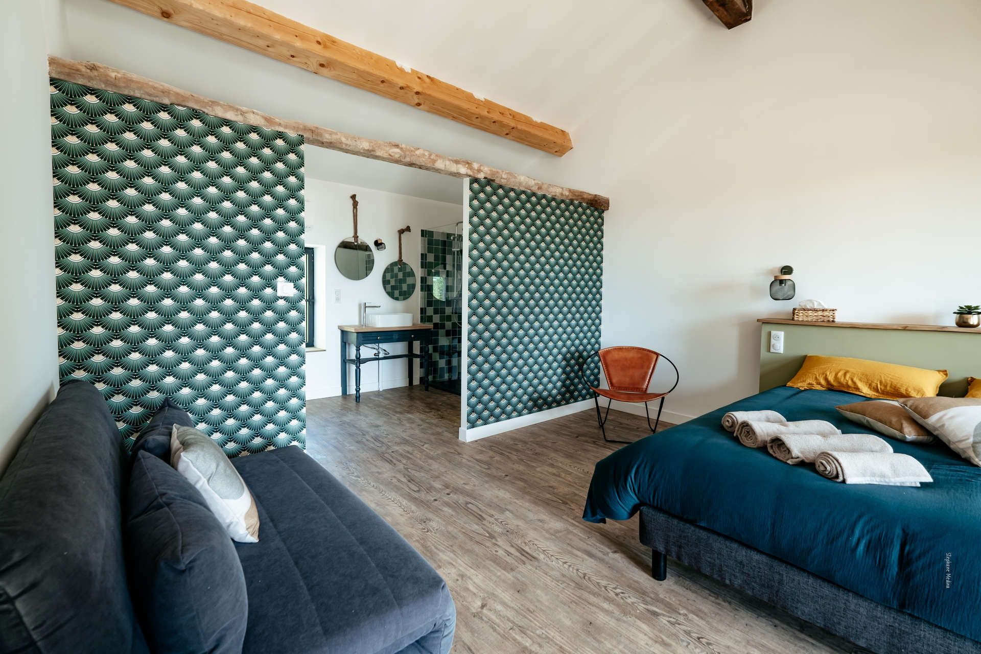 Een slaapkamer met een bed, een stoel, een bureau en een badkamer zichtbaar door een geopende deur.