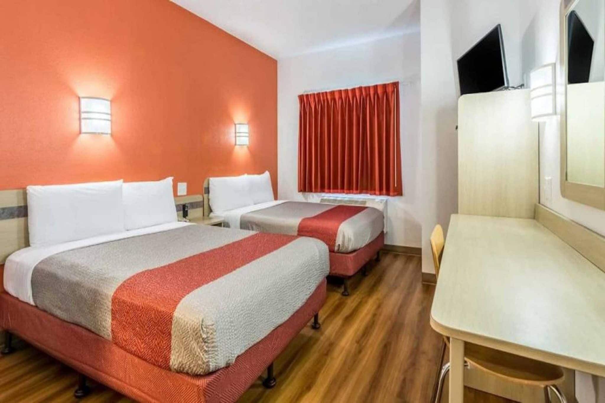 A hotel room with two beds, a desk, and a television.