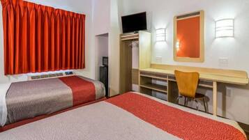 Een hotelkamer met een bed, een bureau met een stoel, een televisie en een kledingkast.