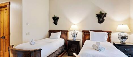 Habitación de hotel con dos camas de madera, mesitas de noche con lámparas y una puerta de madera.