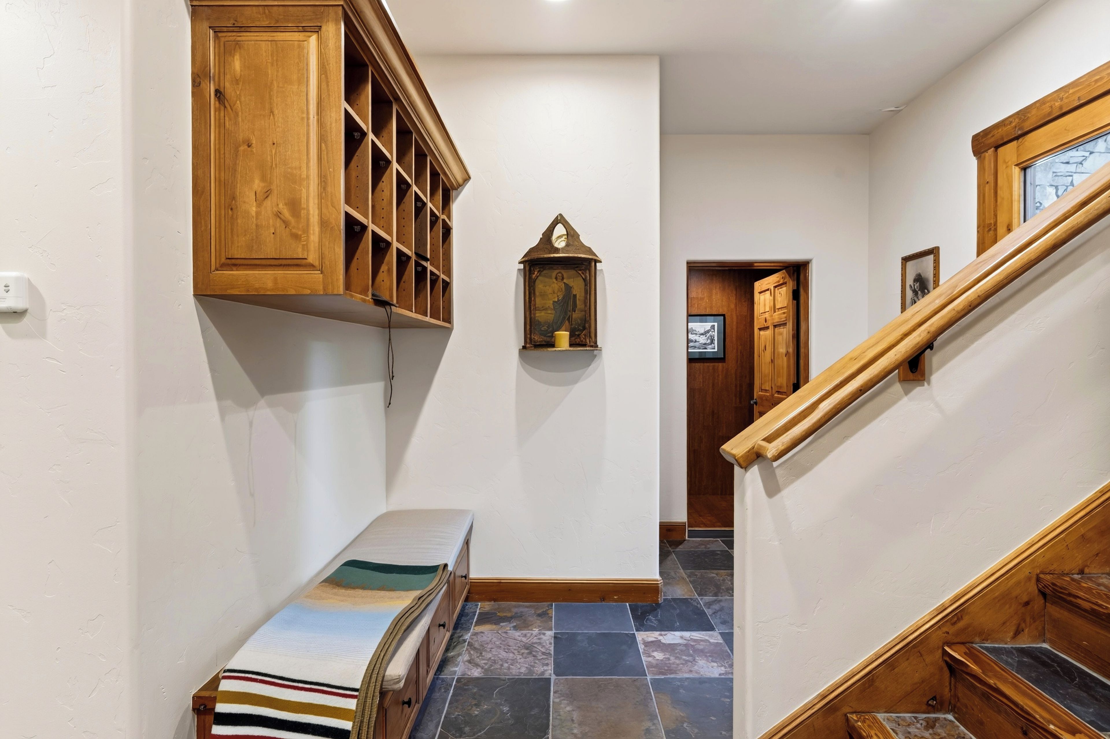 A hallway with a wooden bench, a wall-mounted shelf, and a staircase with wooden railings.