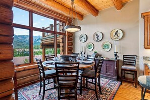 A log cabin interior with a dining area, wooden walls, and a view of mountains. - Log Home • Hot Tub + Full Gym | Ski-in/out Funicular | 115 Tristant (Mountain Village)