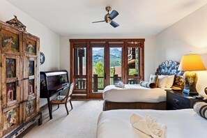 Une chambre d’hôtel équipée d’un lit, d’un bureau, d’une chaise, d’une armoire, d’un ventilateur de plafond et offrant une vue sur les montagnes par les fenêtres.