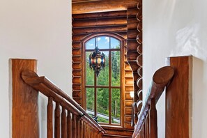 Un escalier en bois offrant une vue sur une forêt, visible à travers une grande fenêtre en arc de cercle.