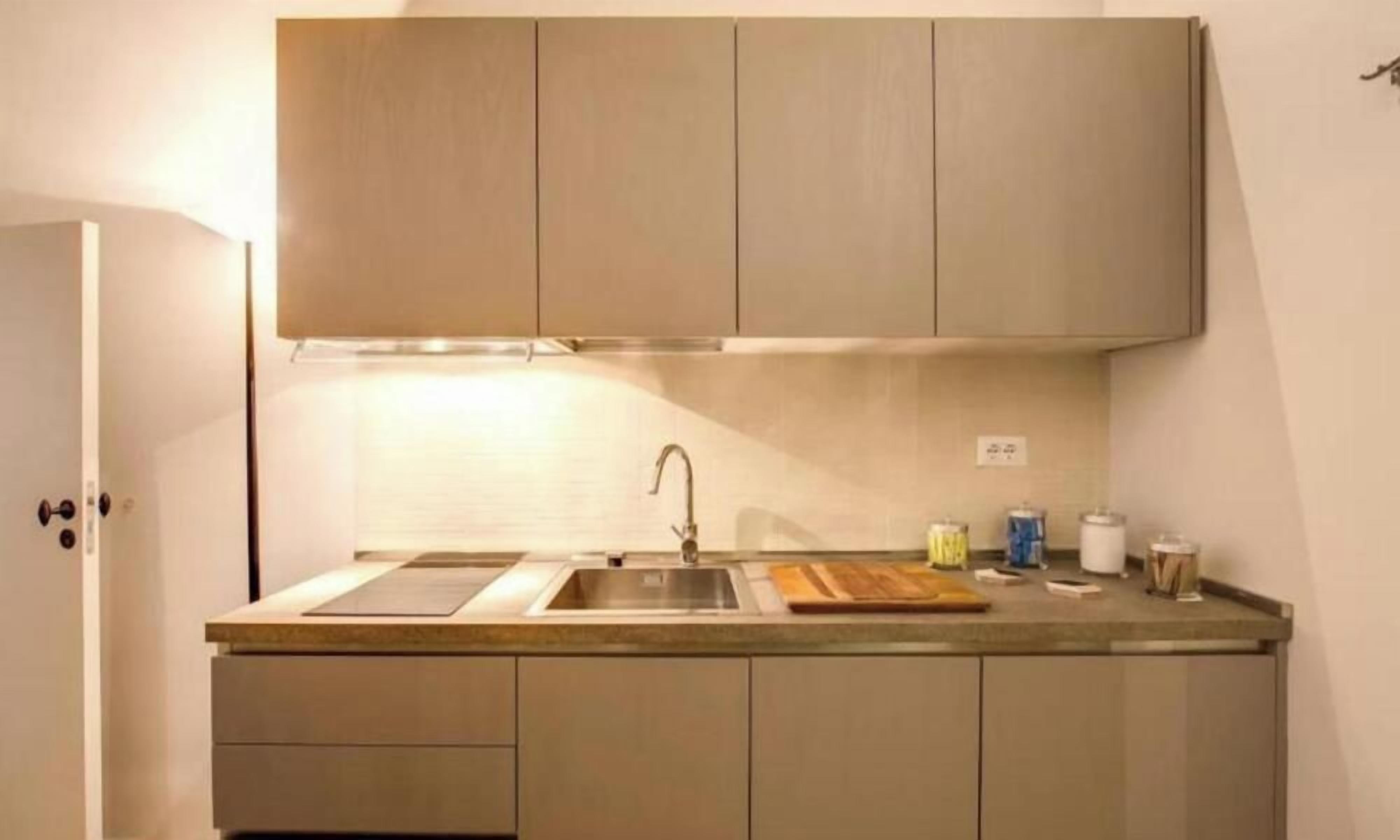 Una cocina compacta con un solo lavamanos, una tabla de cortar de madera y una campana extractora sobre la estufa.