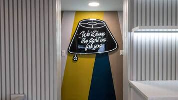 Um corredor com um letreiro de neon na parede e uma porta com estampa listrada.