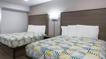 A hotel room with two beds, each with patterned bedding, a wall-mounted air conditioning unit, and a ceiling light.